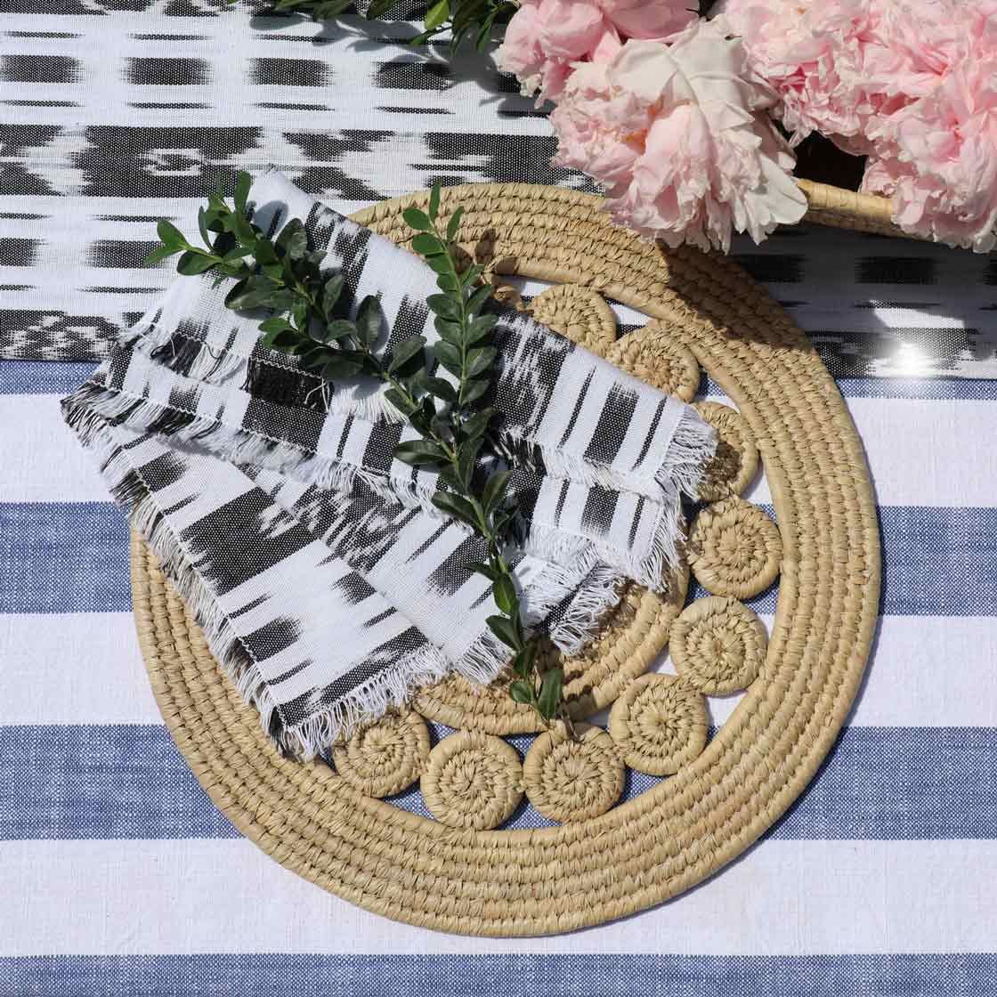 Round woven mat with a black and white patterned towel and pink flowers on a striped fabric background