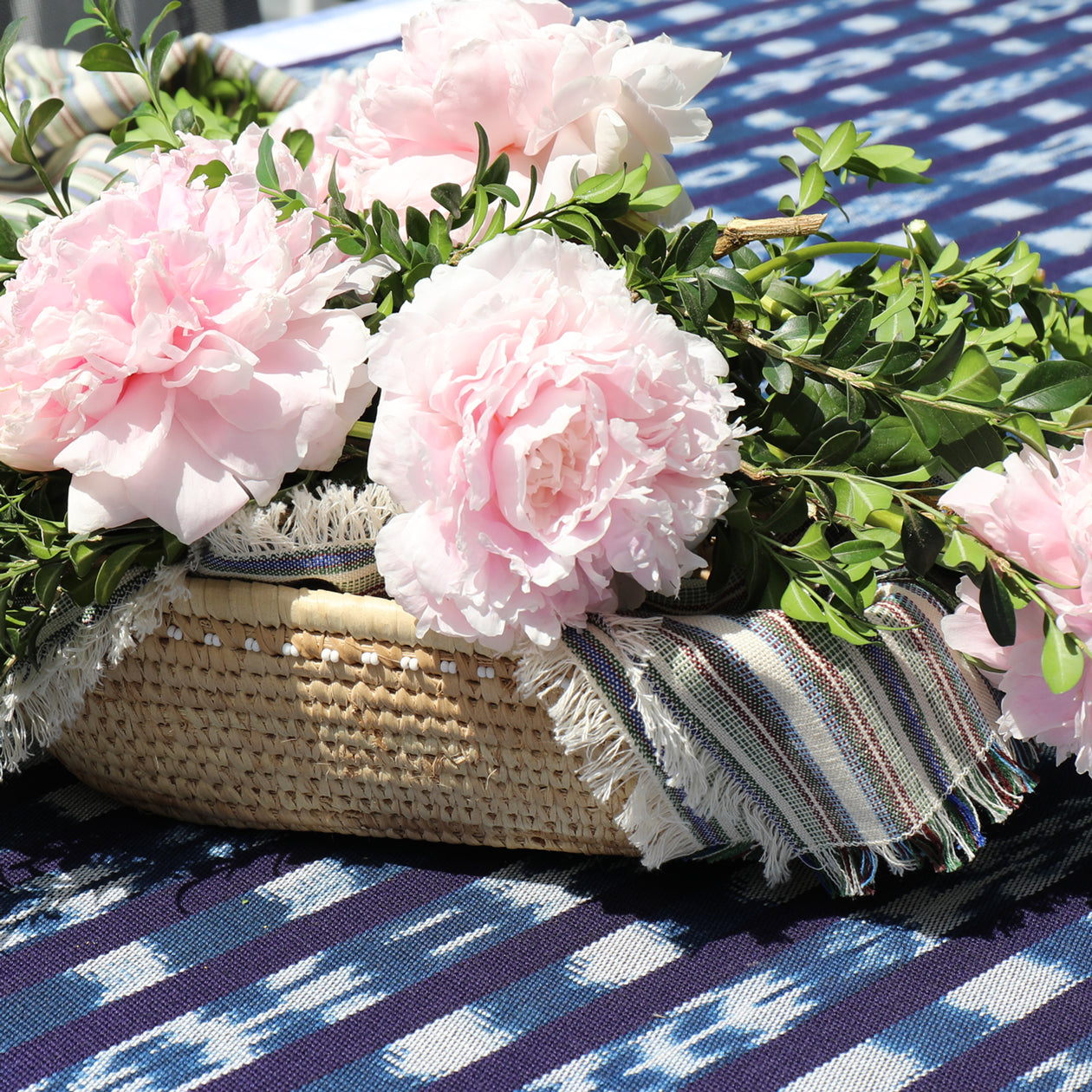 Wicker basket with pink flowers and greenery on a blue and white checkered tablecloth