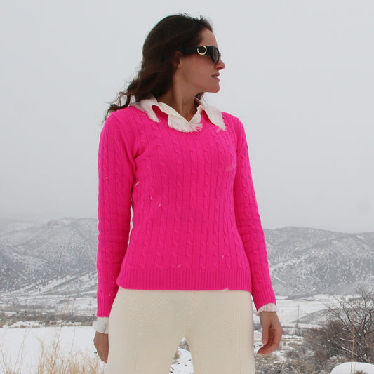 A woman wearing a bright pink cable-knit sweater with a white ruffled collar, paired with cream pants, standing outdoors in a snowy landscape.