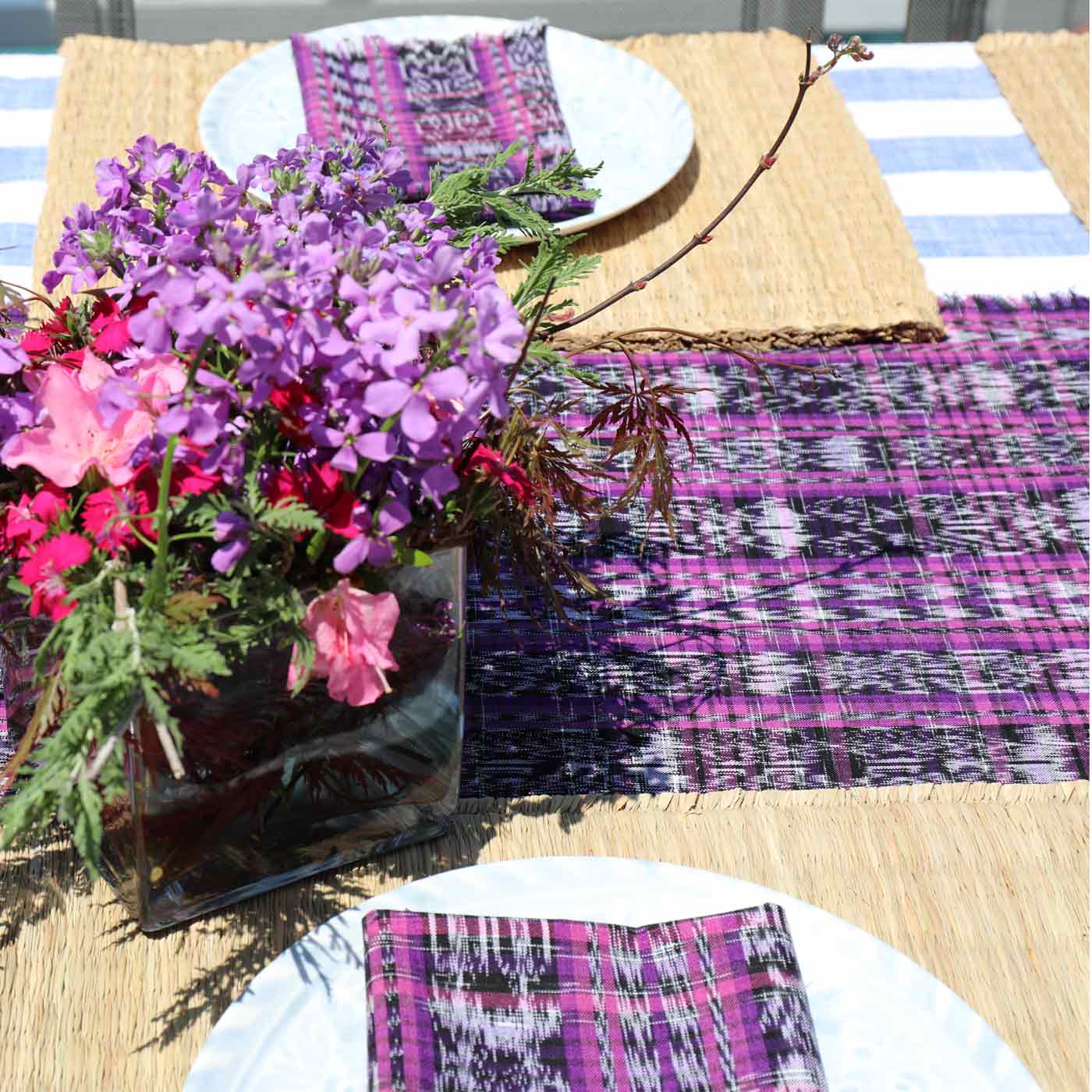 Table setting with purple and pink flowers, plaid napkins, and a striped tablecloth.