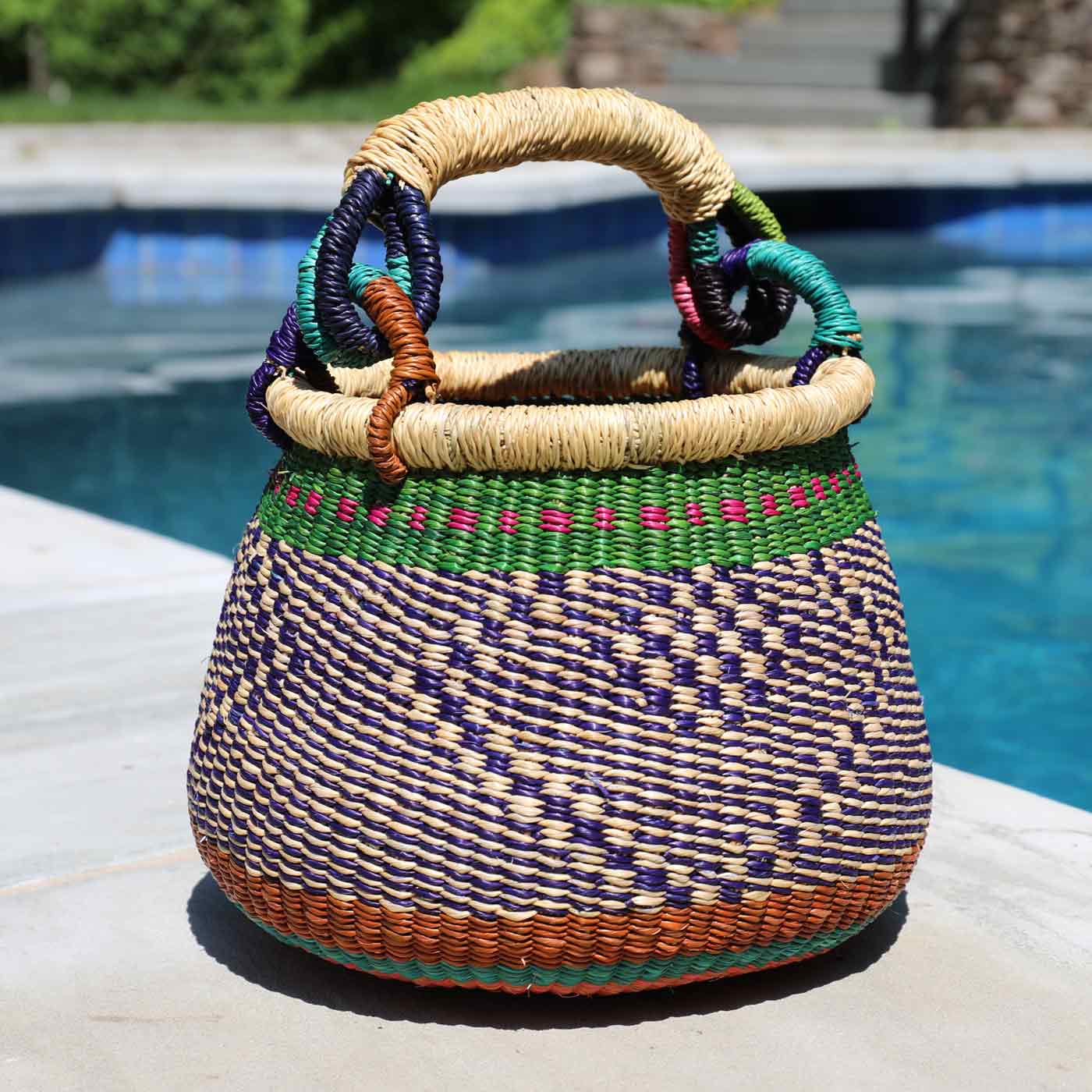 Woven basket with colorful handles on a poolside surface