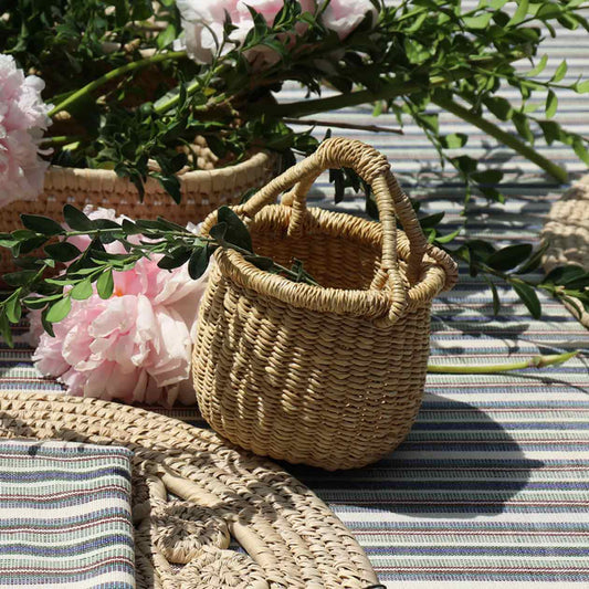 Woven basket on a striped surface with pink flowers and greenery.
