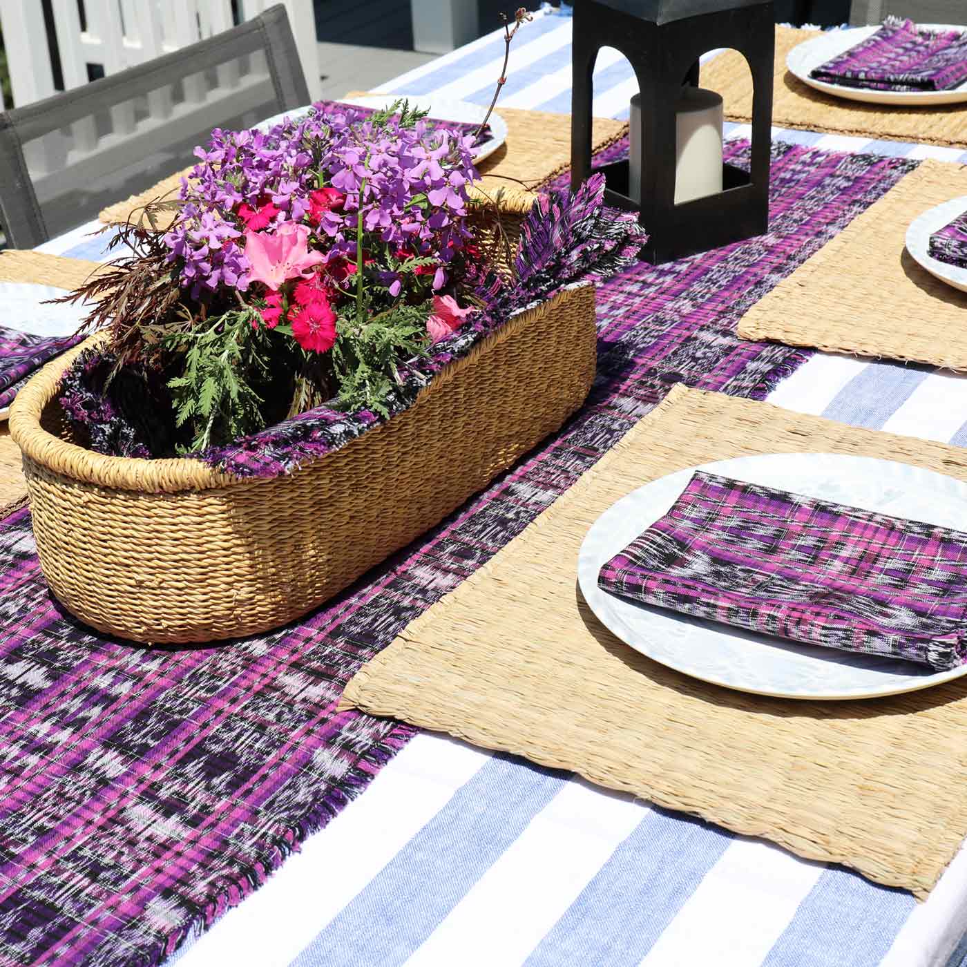 Outdoor table setting with a woven basket of flowers, striped tablecloth, and plaid napkins.
