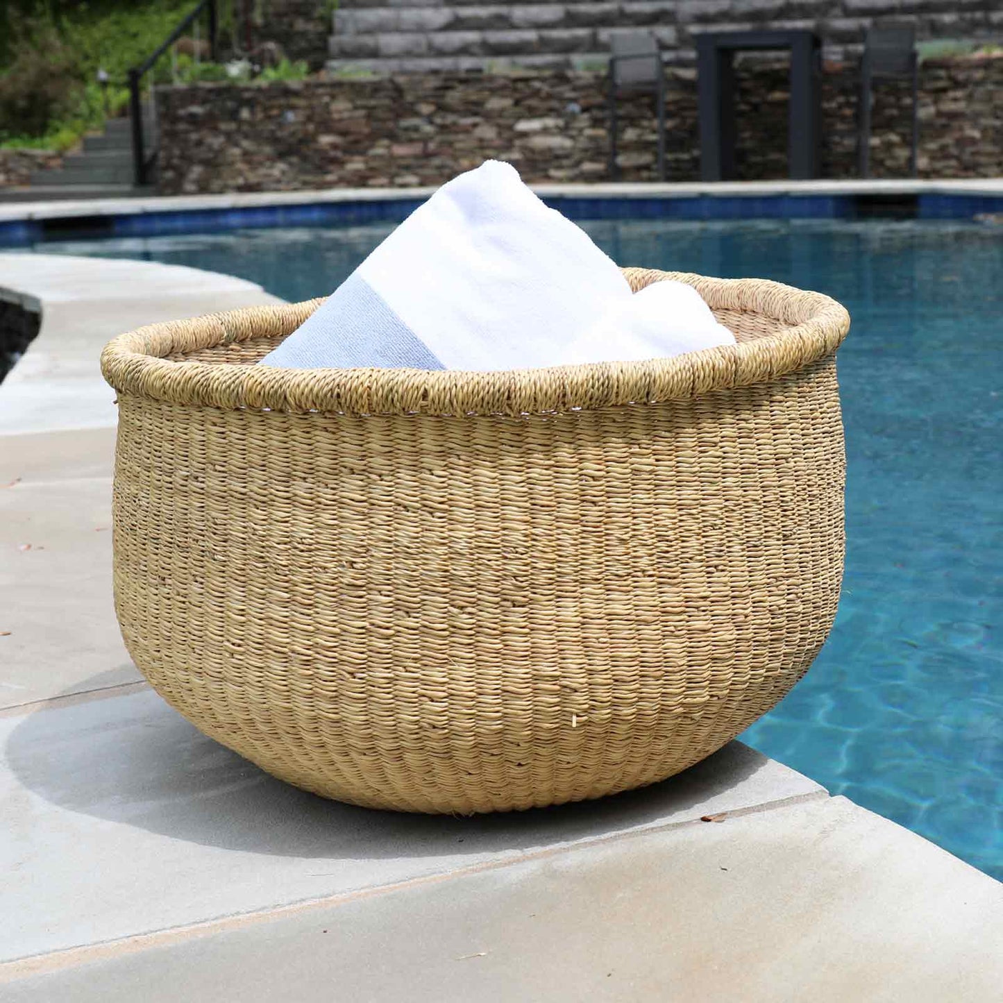 Woven basket with white towels on a poolside ledge