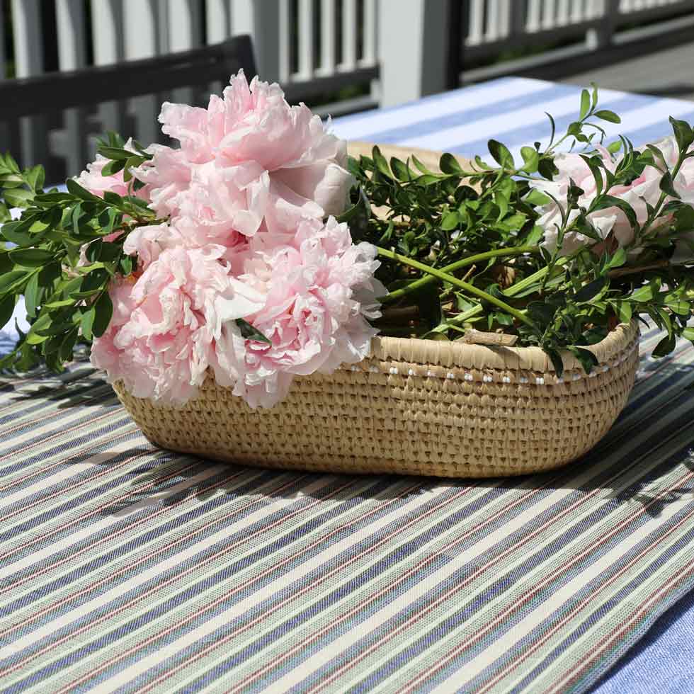 Wicker basket with pink flowers on a striped tablecloth. long-narrow-serving-basket-table-center-piece