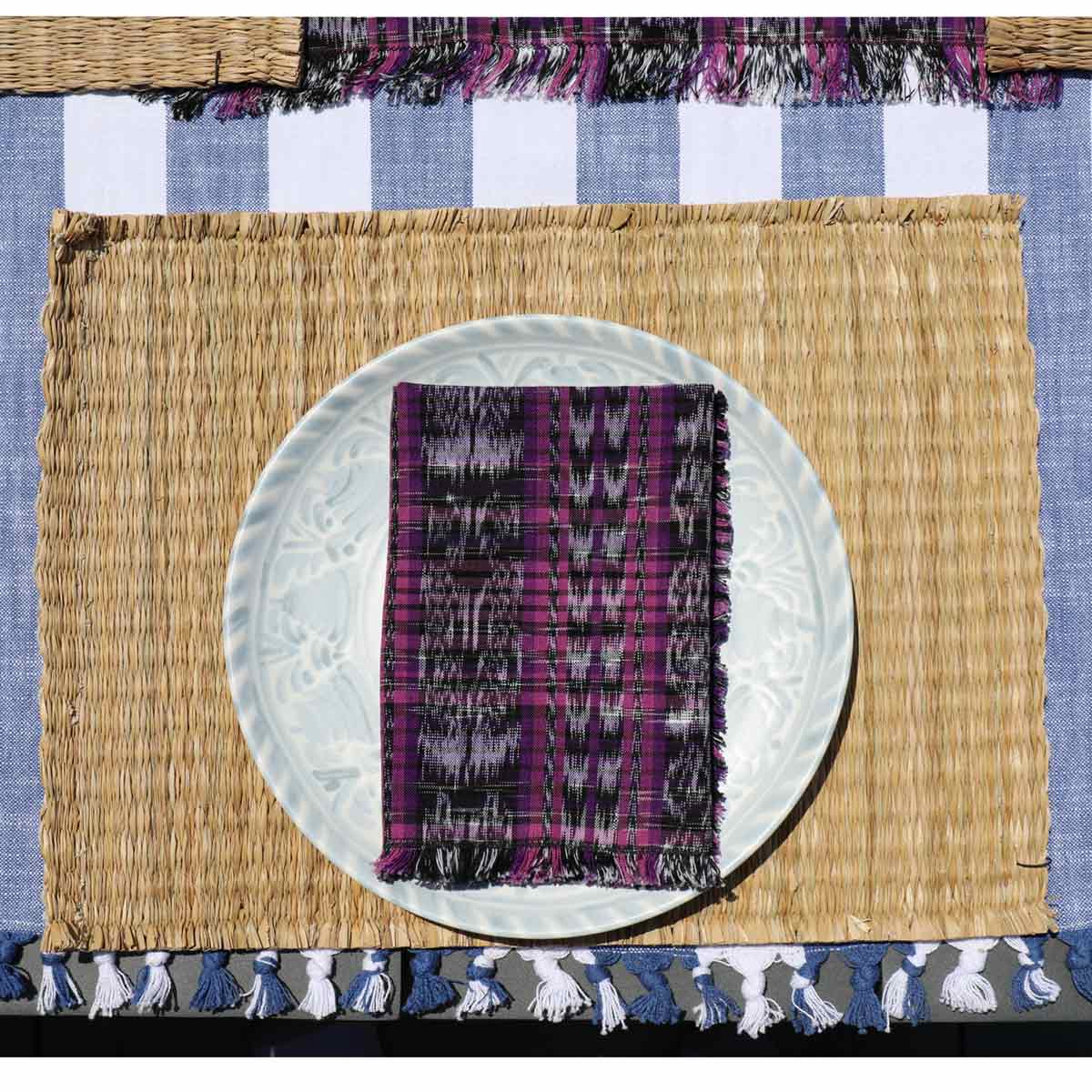 Placemat with woven texture and purple patterned napkin on a blue and white checkered tablecloth.