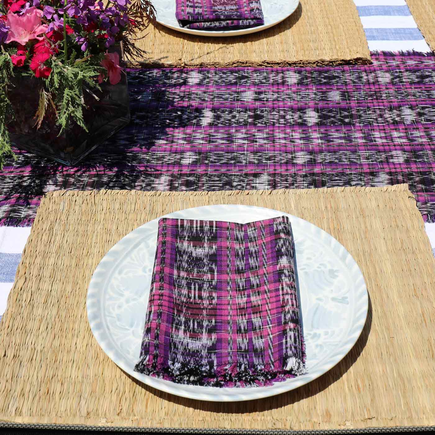 Placemat with purple and black pattern on a woven mat with flowers in the background