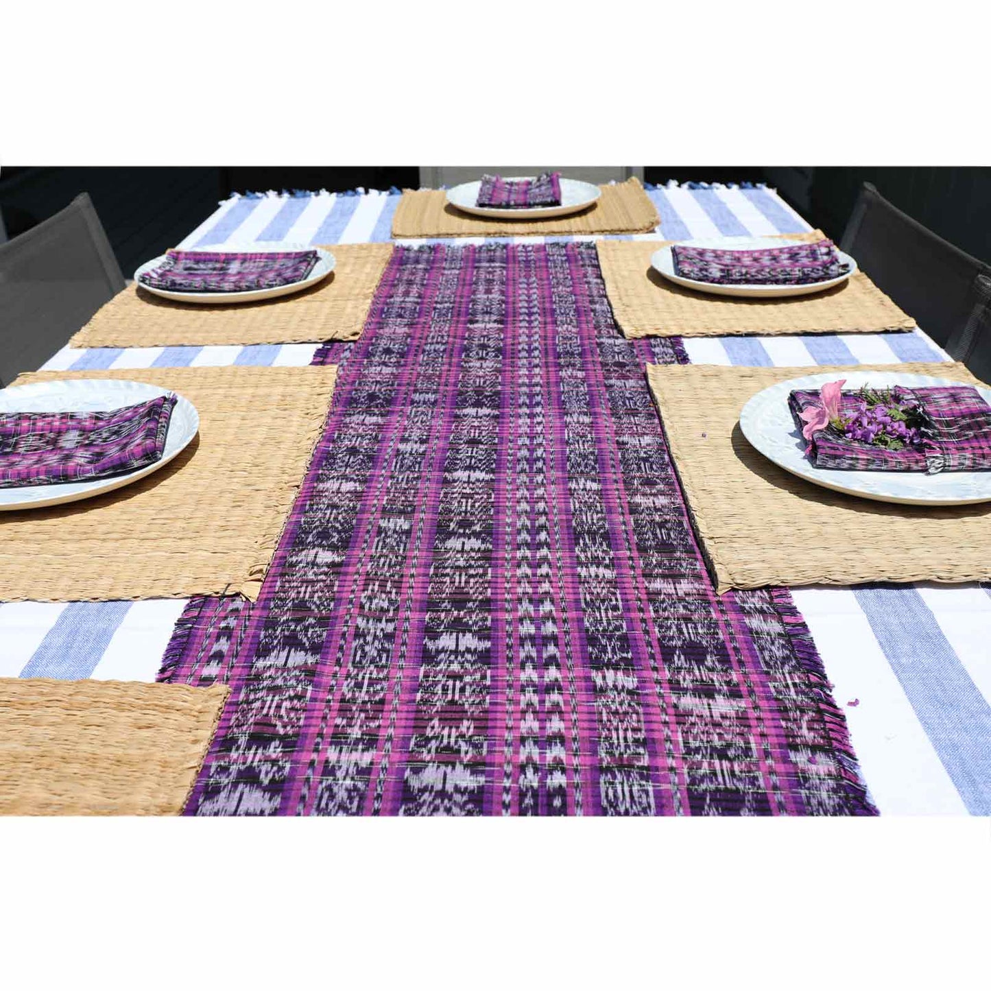 Table setting with a purple and white patterned table runner, plates, and napkins on a striped tablecloth.