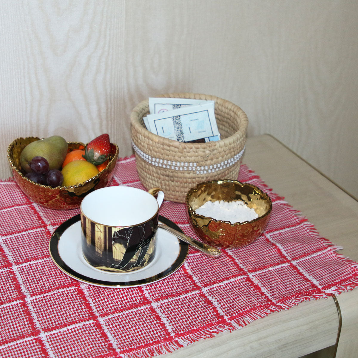Teacup, saucer, and decorative bowl on a red checkered tablecloth with a woven basket in the background.