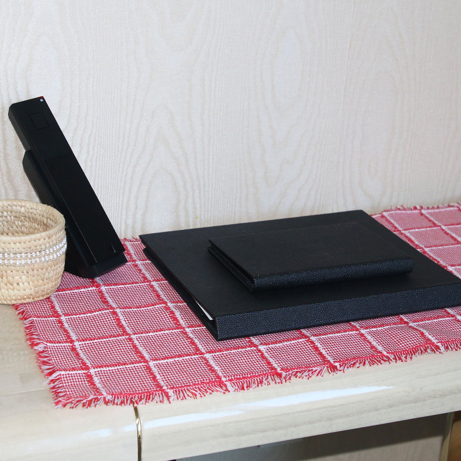 Black folders on a red checkered tablecloth with a white textured wall in the background