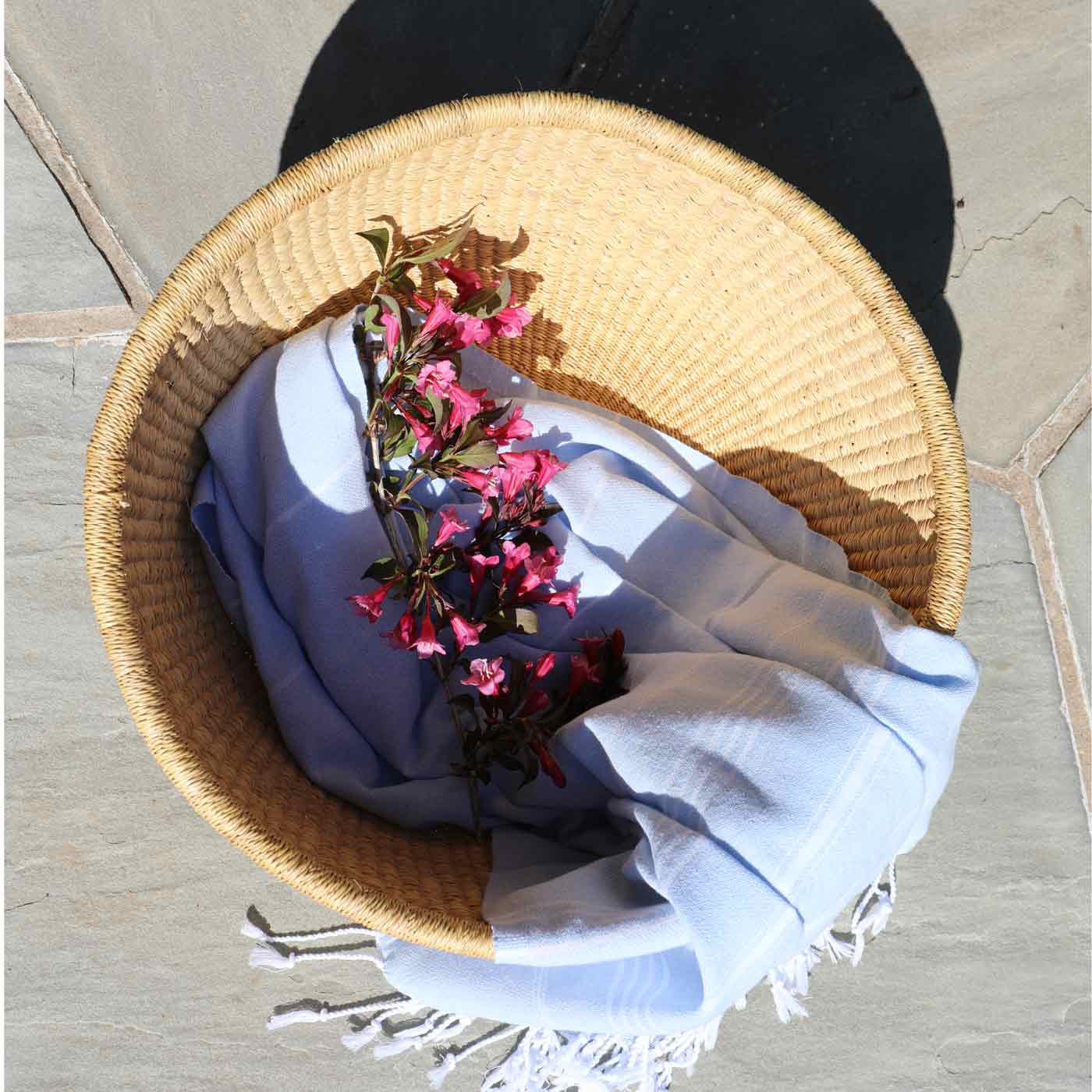 Woven basket with a blue towel and pink flowers on a stone surface