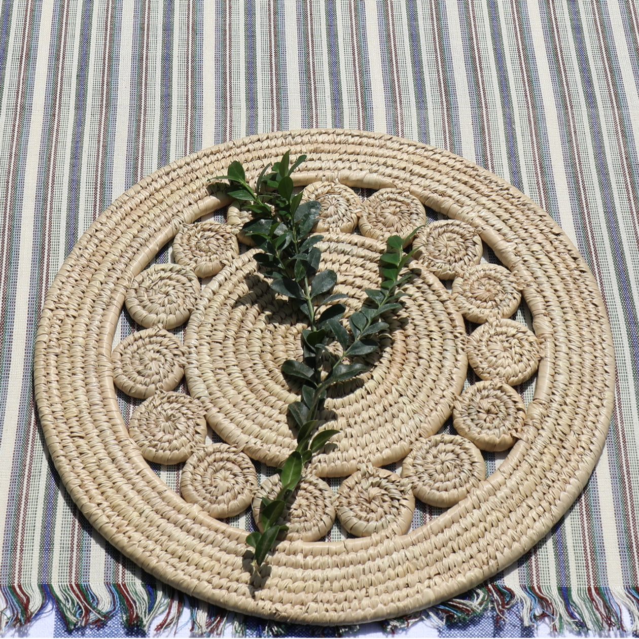 Round woven mat with a leafy branch on a striped fabric background