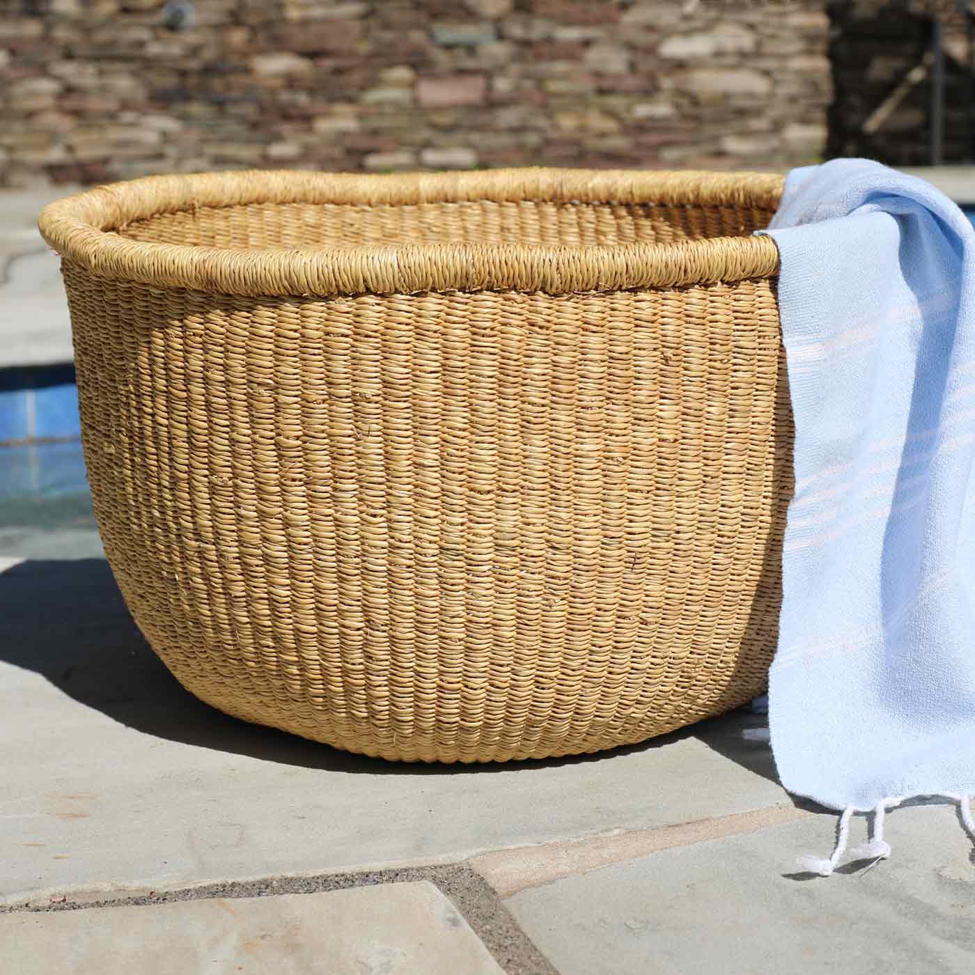 Woven basket on a stone patio with a stone wall and pool in the background
