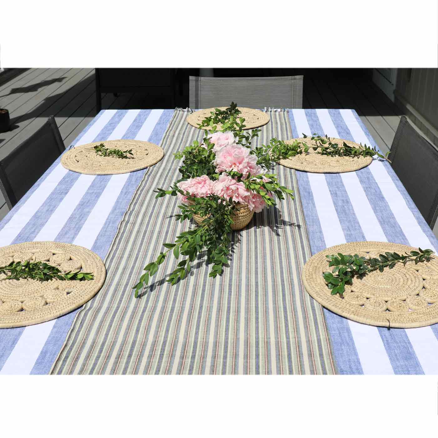 Table setting with striped tablecloth, floral centerpiece, and woven placemats.
