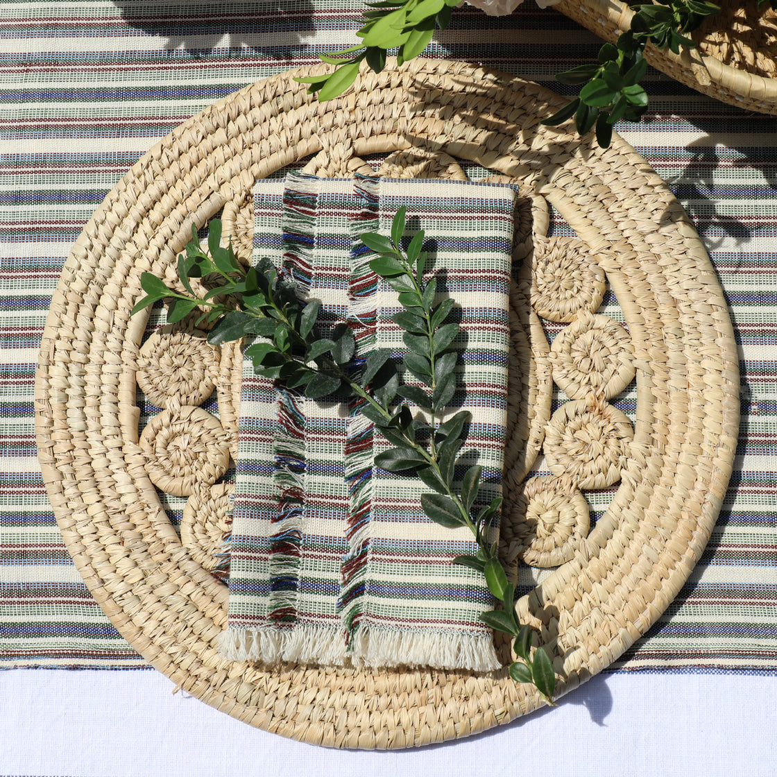 Woven placemat with striped napkin and greenery on a striped surface